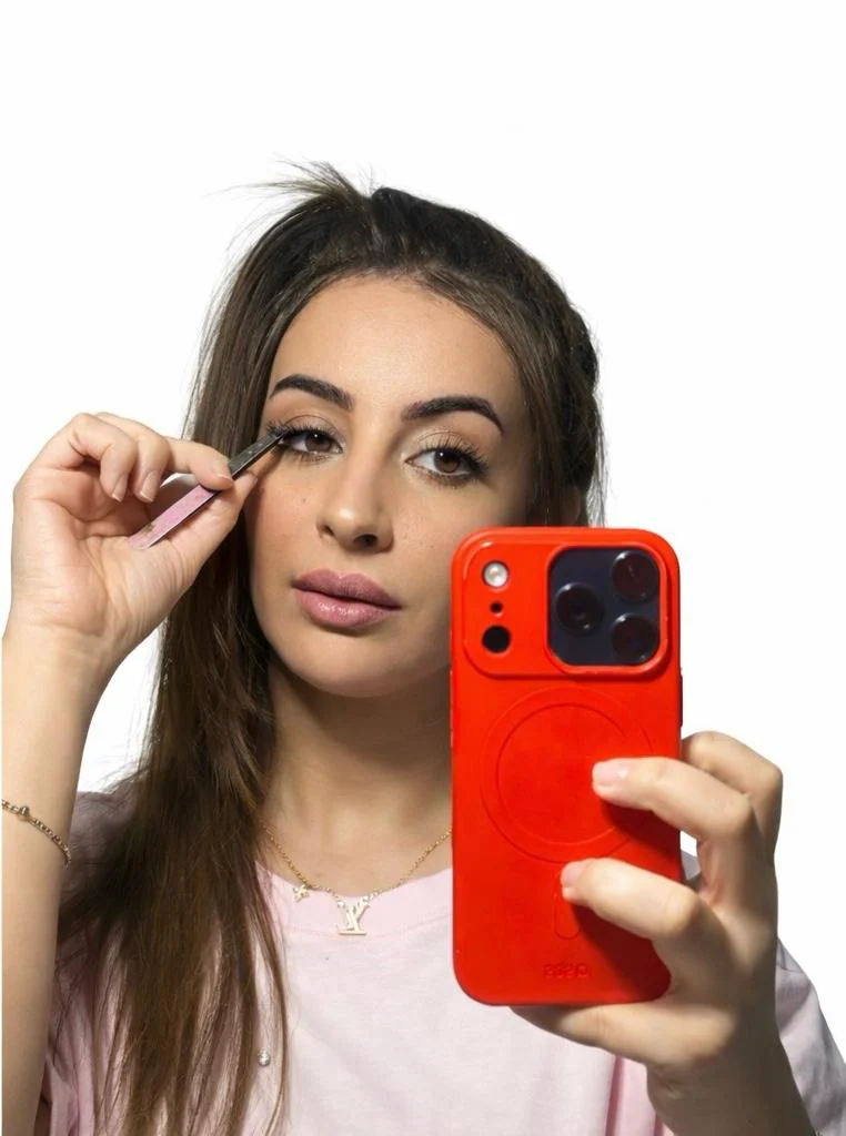 Model applying lashes in mirror with red phone case